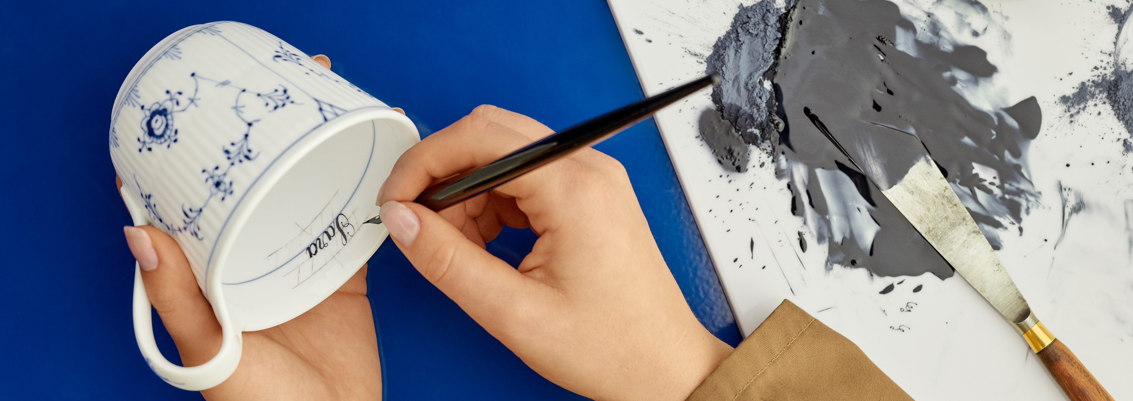 En blåmaler er i gang med at male et navn i en Musselmalet Riflet Højhankskop